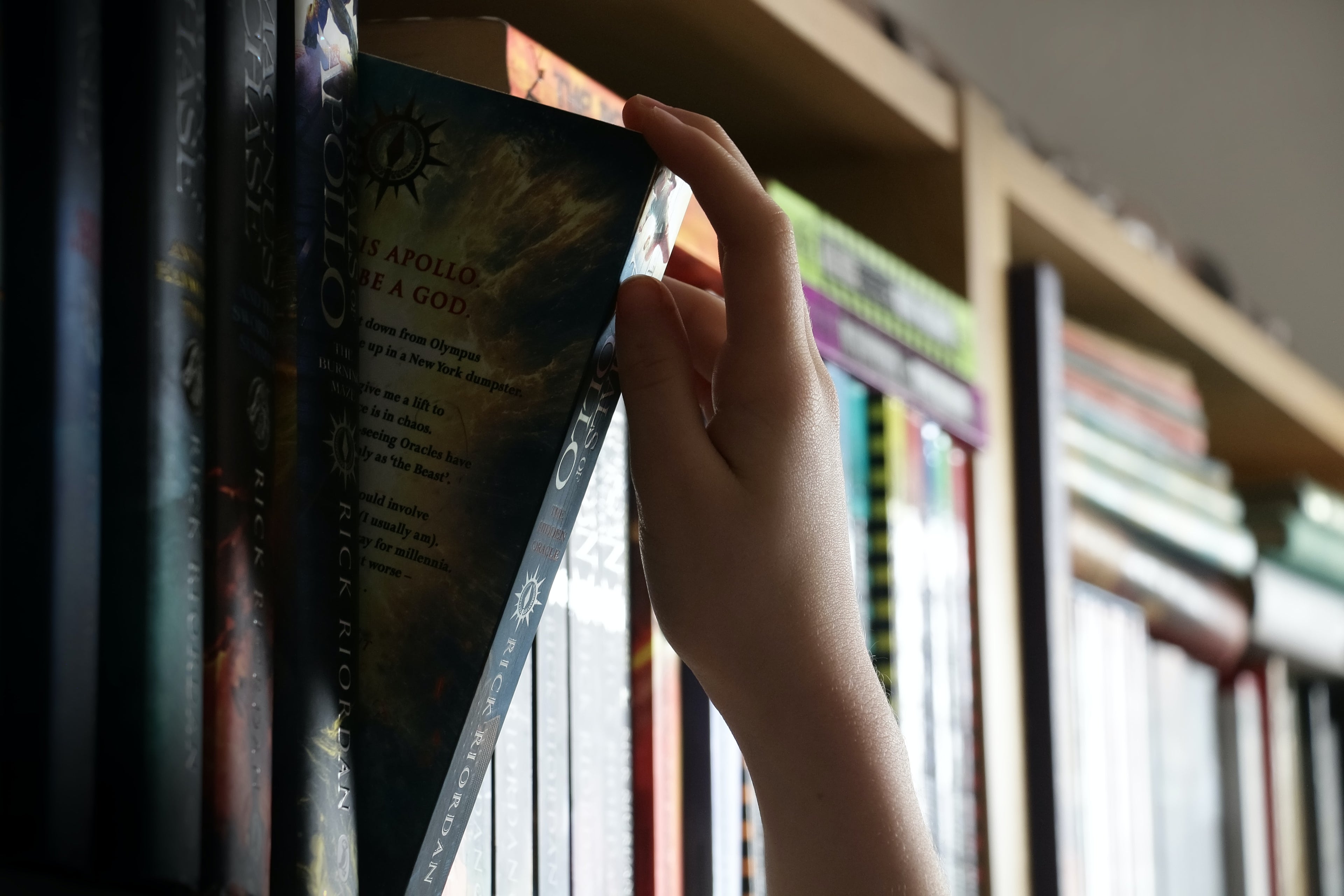 Book case packed with book, young hand reaching up to pull one book out